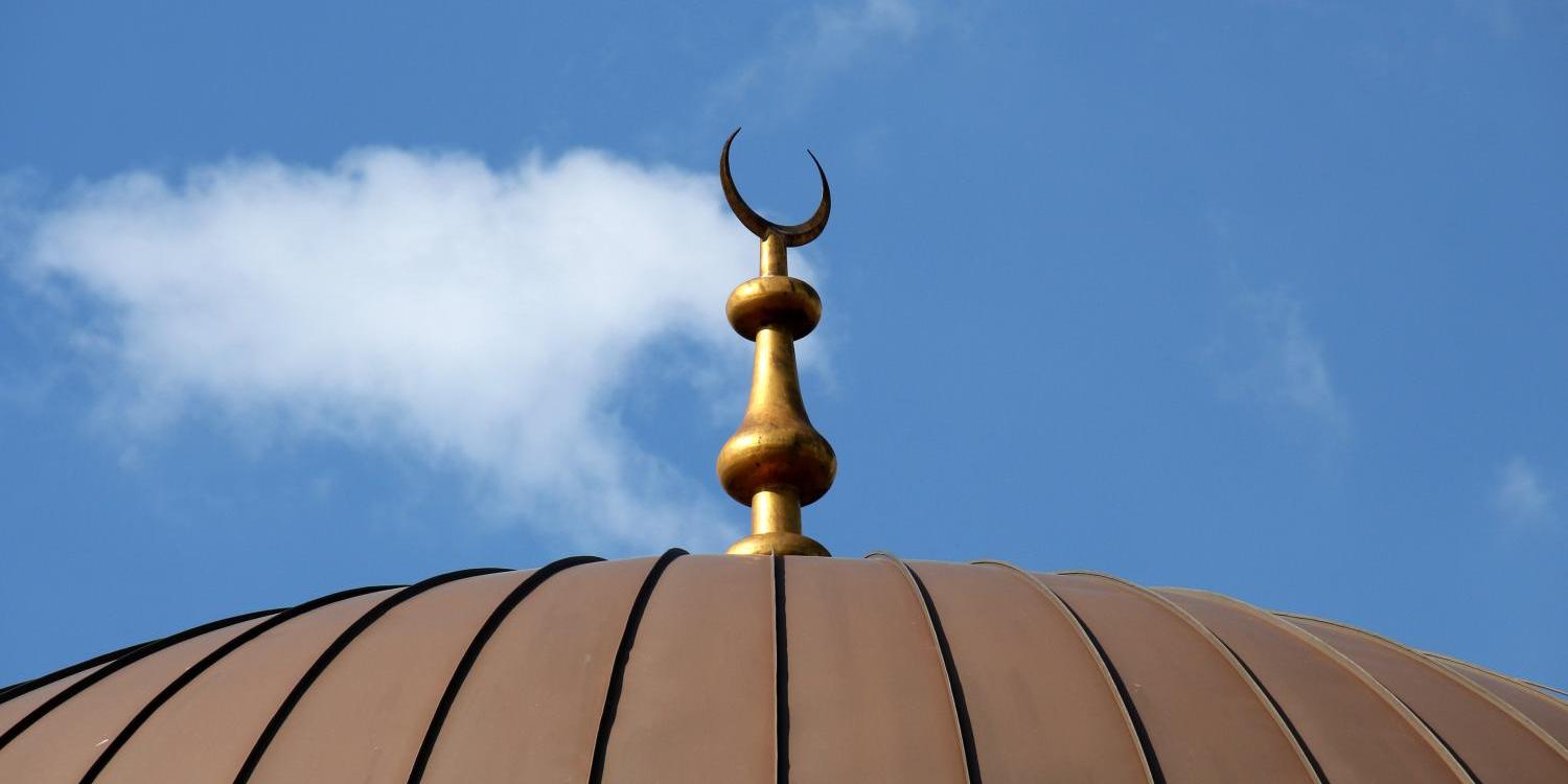 Oberer Teil der Kuppel einer Mosche, darauf ein Halbmond vor dem Himmel.