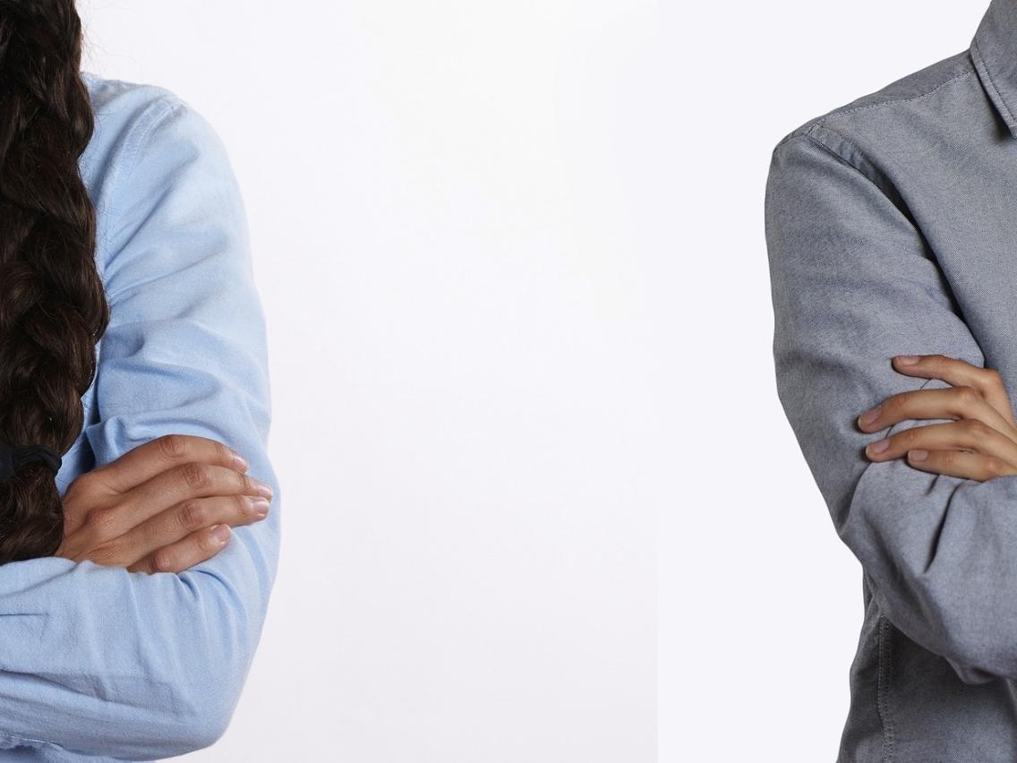 Zwei Menschen stehen mit verschränkten Armen mit größerem Abstand nebeneinander. Man sieht, dass es eine Frau (links) und ein Mann (rechts) ist, aber kein Gesicht.