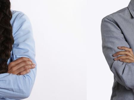 Zwei Menschen stehen mit verschränkten Armen mit größerem Abstand nebeneinander. Man sieht, dass es eine Frau (links) und ein Mann (rechts) ist, aber kein Gesicht.