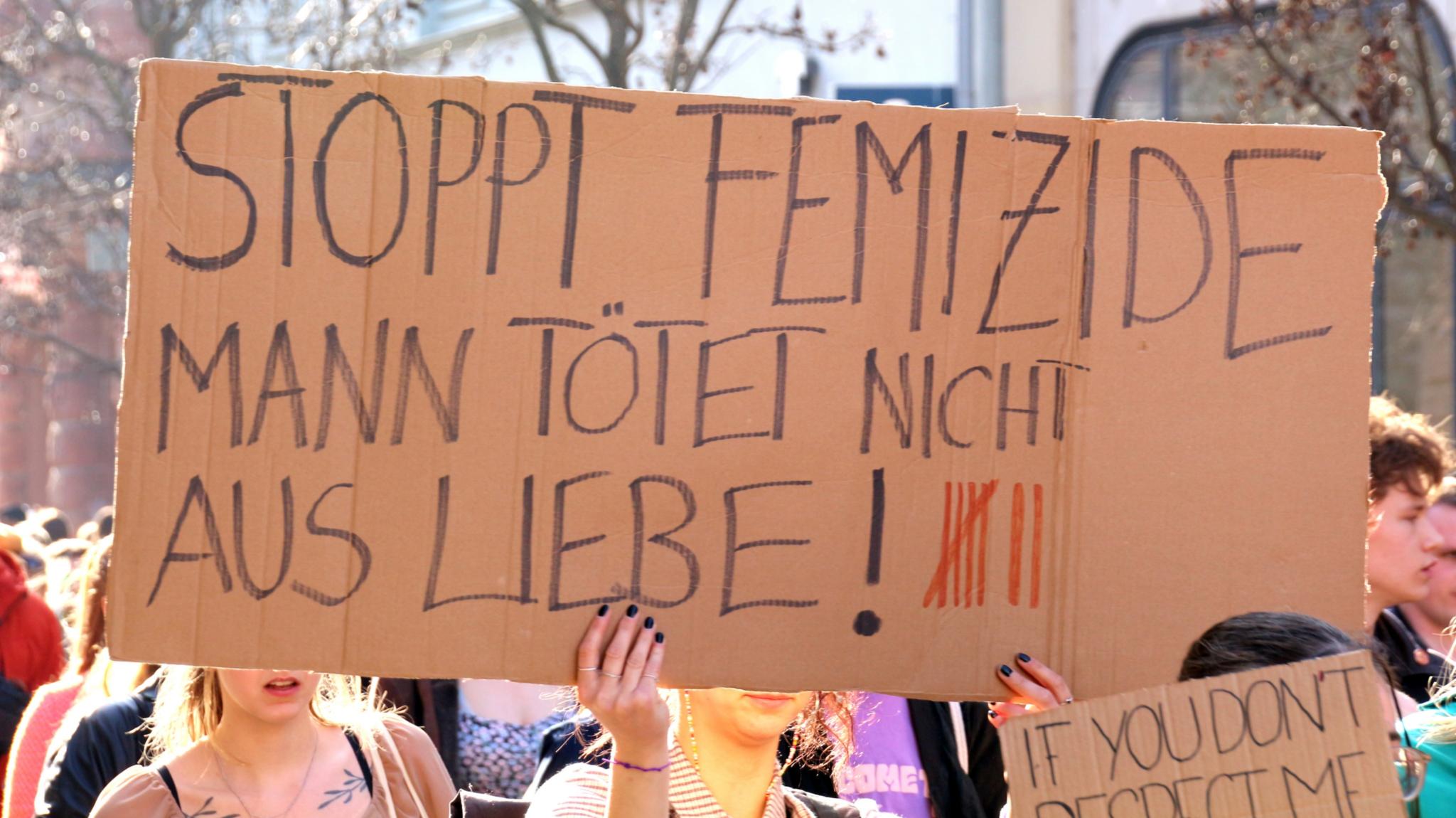 Handgeschriebenes Plakat mit dem Text: 'Stoppt Femizide - Mann tötet nicht aus Liebe!