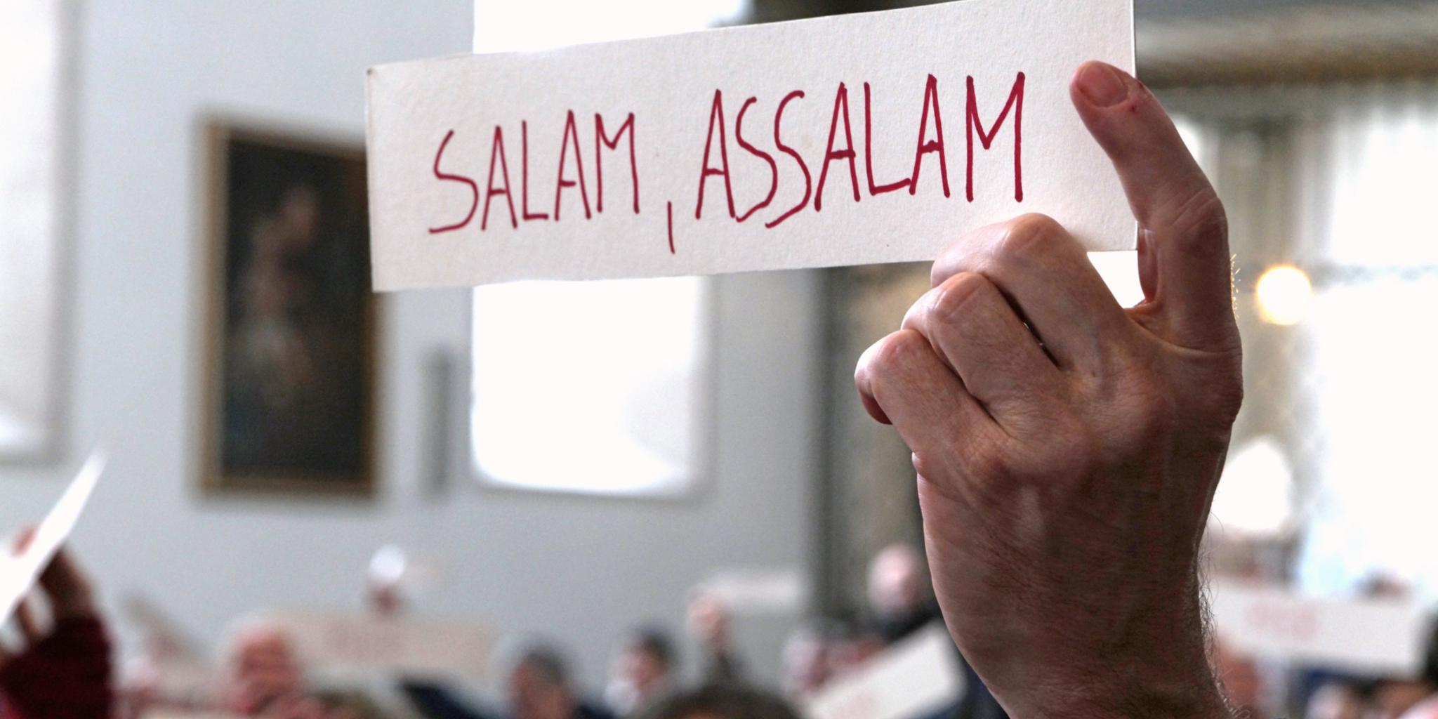 Hand hält Schild mit der Aufschrift 'Salam, assalam'