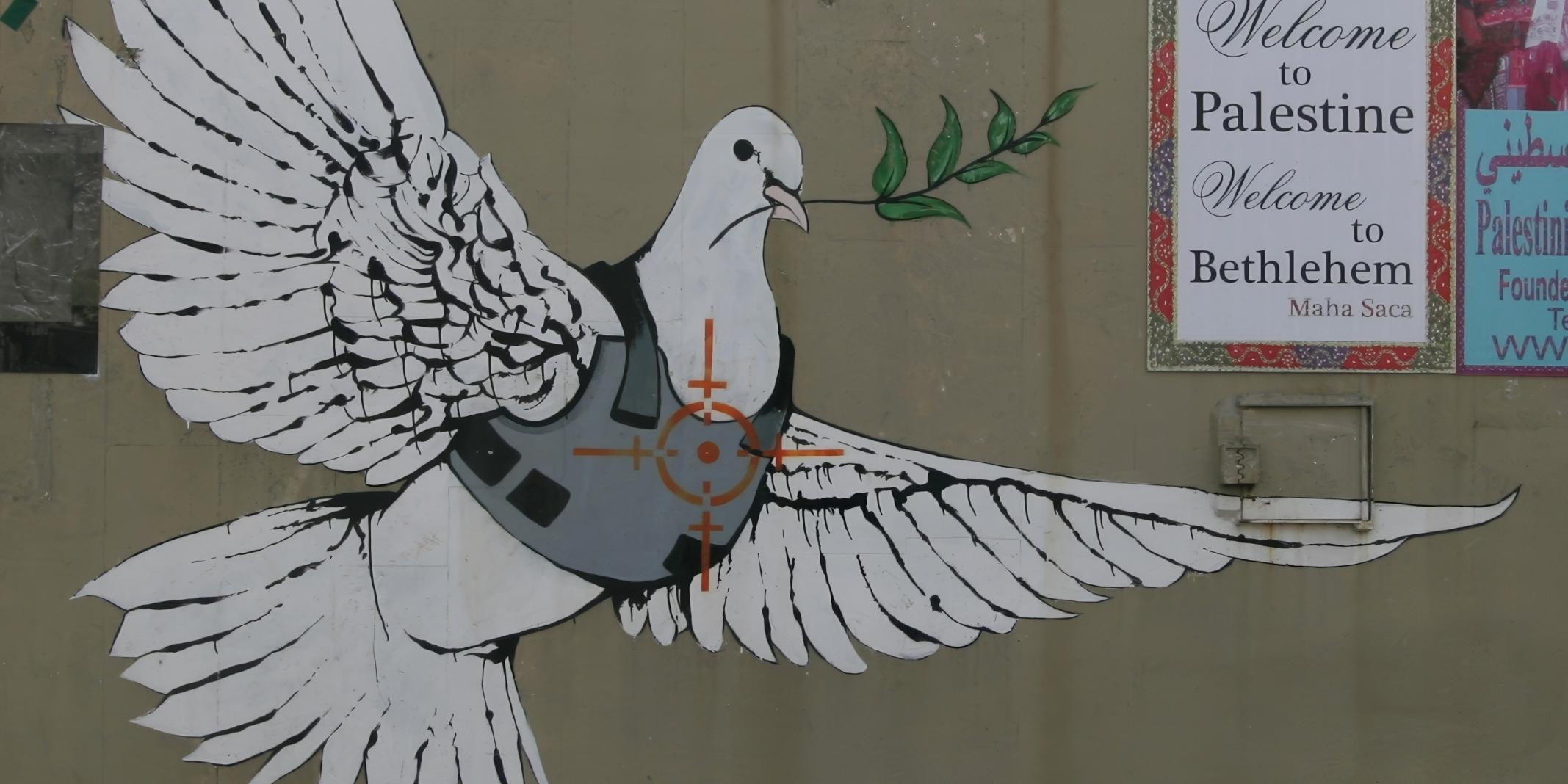 Wandgemälde: eine weiße Taube in einer kugelsicheren Weste mit einem Olivenzweig, gemalt auf einer Souvenirladenwand.
