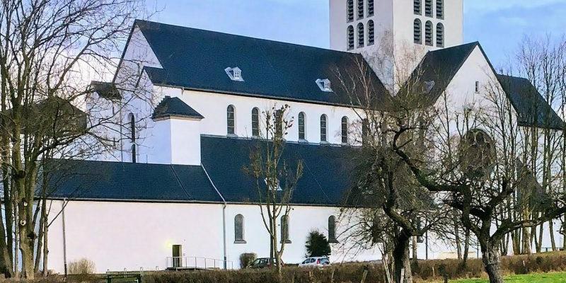 Ein Klostergebäude mit Kirchenschiff und Kirchturm inmitten eines Gartens mit einem kleinen Weiher davor.