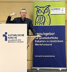 Ein Mann steht an einem Rednerpult, es ist Dr. Martin Barth von der Görres-Gesellschaft in Bonn. Hinter ihm ein Rollup mit einer gezeichneten Eule aus dem Logo der Goerres-Gesellschaft.