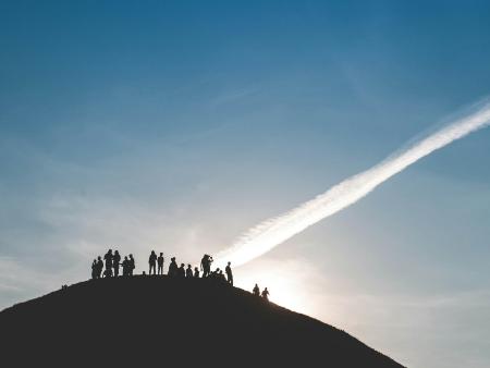 Eine Gruppe von Menschen steht auf einem Hügel und schaut in den Himmel.