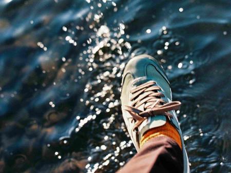 Ein Fuß mit einem Turnschuh schwebt über einer glitzernden Wasseroberfläche, als wolle er gleich darauftreten.