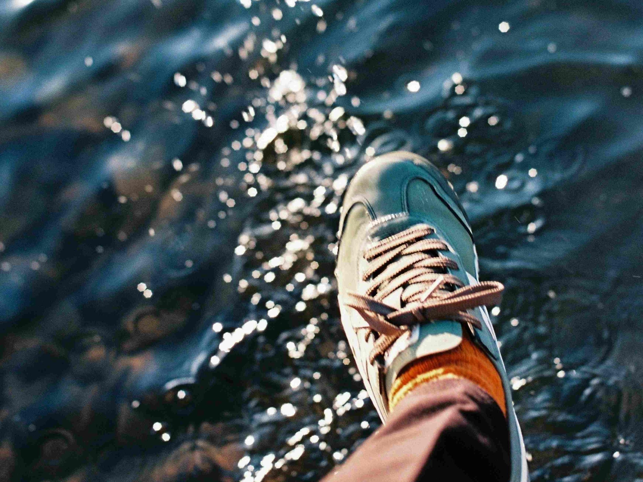 Ein Fuß mit einem Turnschuh schwebt über einer glitzernden Wasseroberfläche, als wolle er gleich darauftreten.