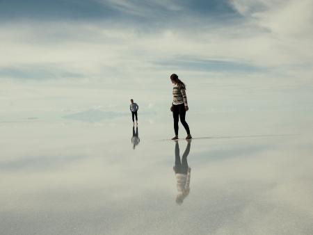 Zwei Personen gehen wie auf Wolken, blicken sich an, sie spiegeln sich im Untergrund.