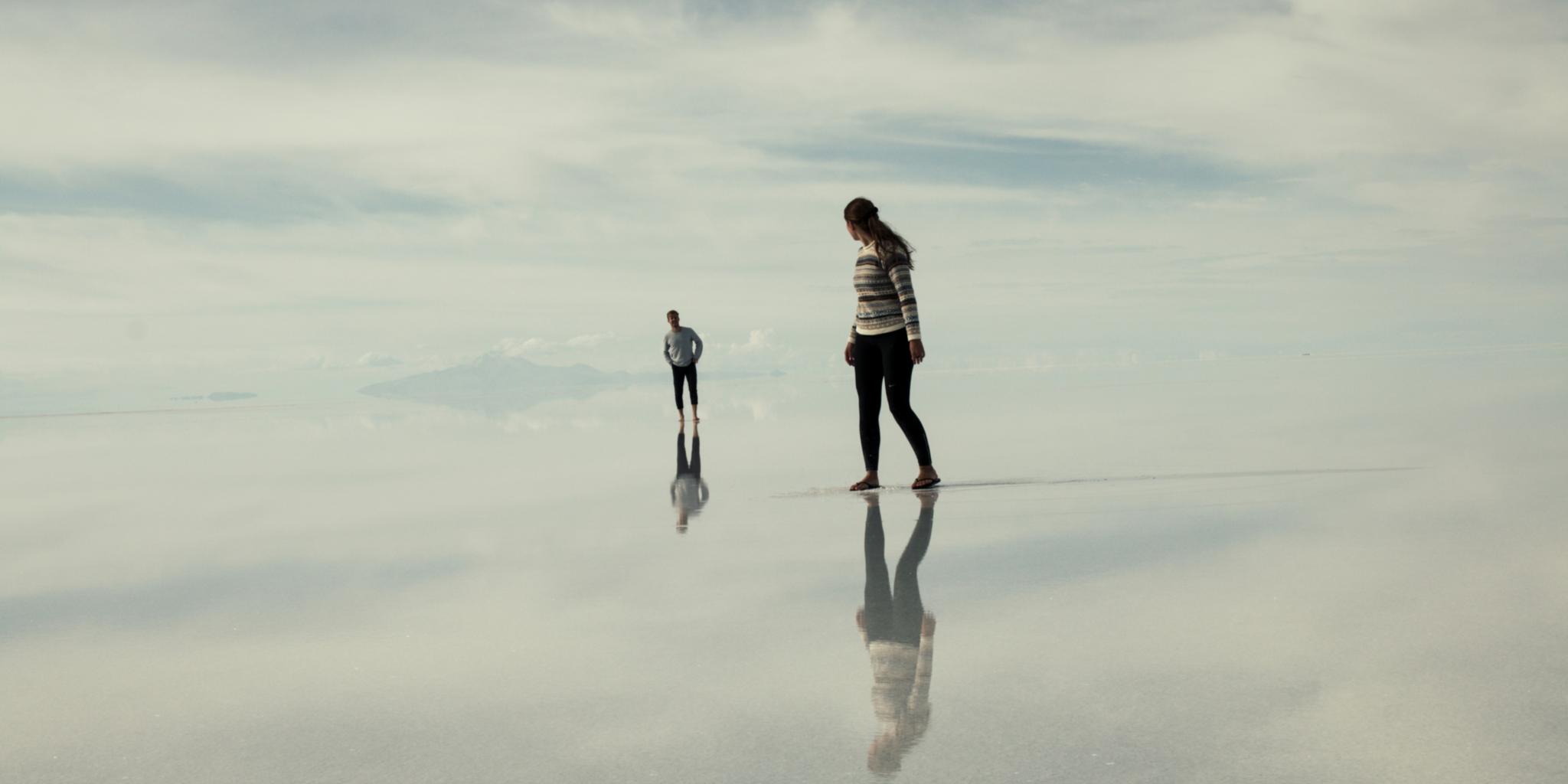 Zwei Personen gehen wie auf Wolken, blicken sich an, sie spiegeln sich im Untergrund.