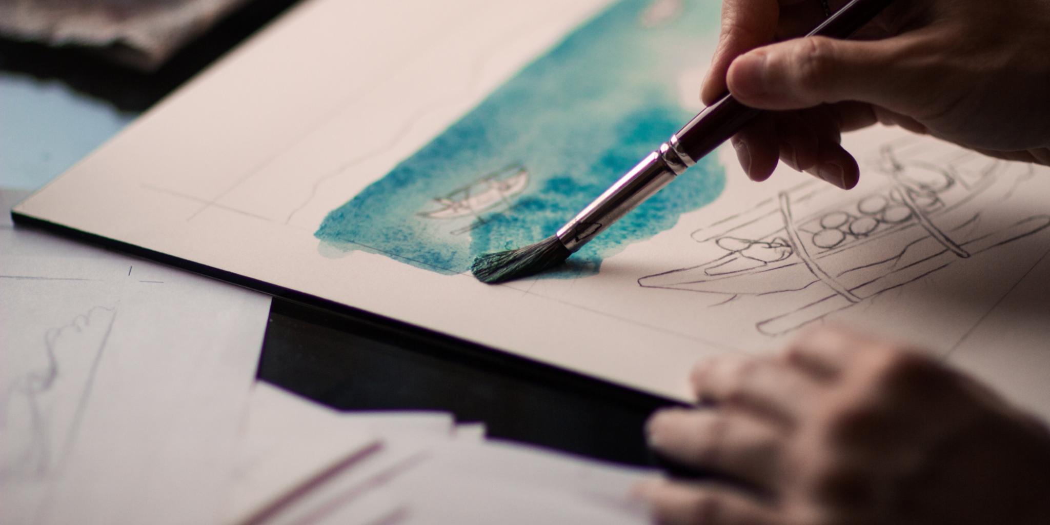 Hand einer Frau, die ein Aquarell malt.